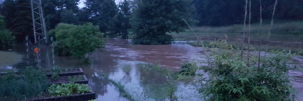 Auf dem Bild sieht man einen Fluß, der über die Ufer getretten ist und alles überschwemmt Hochwasser