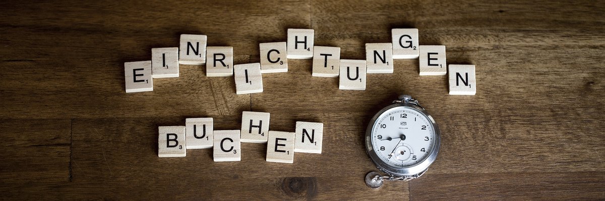 Auf einer Holzplatte liegt der Schriftzug Einrichtung buchen und eine Taschenuhr